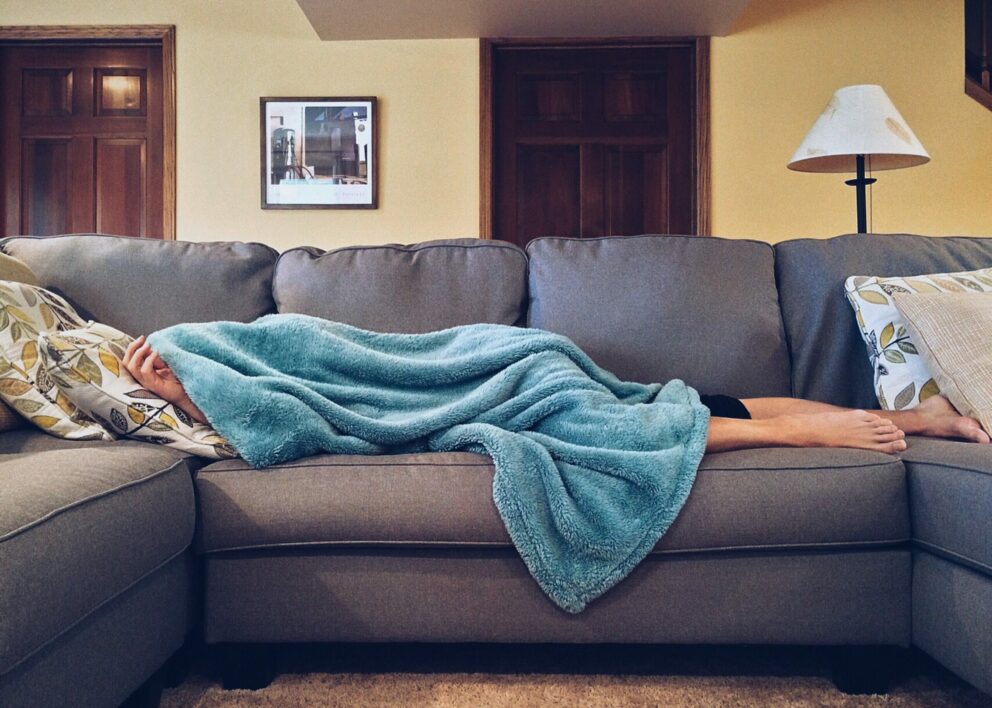 persona sdraiata sul divano e nascosta da una coperta